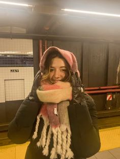 a woman standing on a subway platform wearing a hat and scarf