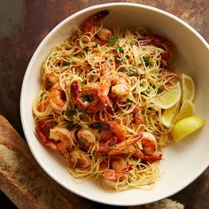 a white bowl filled with pasta and shrimp on top of a table next to bread