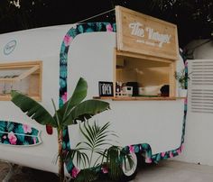 a small food truck parked on the side of a road next to a palm tree