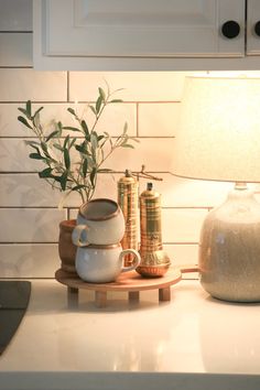 a white kitchen counter top with a lamp and some tea cups on the tray next to it