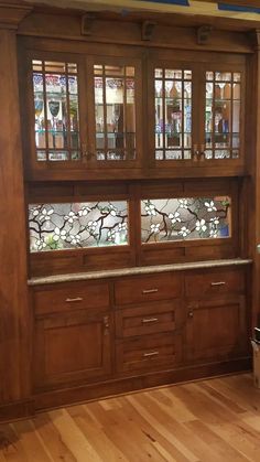 a wooden cabinet with stained glass doors and drawers in a room that has hard wood flooring