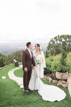 a bride and groom standing on the grass in front of an outdoor ceremony area with greenery