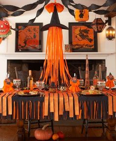 an orange and black halloween table setting with decorations on the mantle, pumpkins hanging from the ceiling