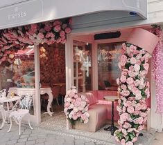 a store front with pink flowers on the outside and tables, chairs, and umbrellas