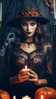 a woman wearing a witches hat and holding a lit candle in her hands with candles around her