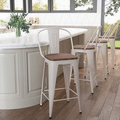 three white stools sit in front of a kitchen island with two vases on it