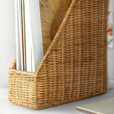 a wicker basket with magazines in it sitting on a table next to a notebook