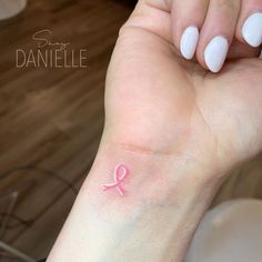 a woman's hand with a pink ribbon tattoo on her left wrist and the word, danielle