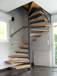 a spiral staircase in a house with tile flooring and gray walls, next to a window