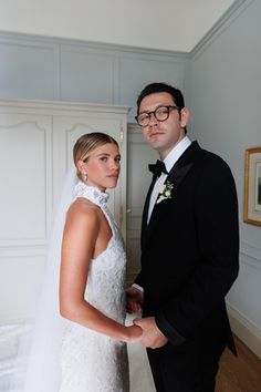 a man and woman standing next to each other in front of a white wall wearing glasses