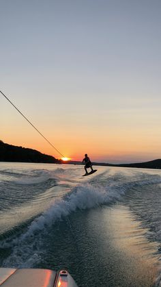 a person on a surfboard riding in the water at sunset or dawn, while someone is being pulled by a boat