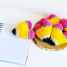 two crocheted stuffed animals sitting on top of a wooden plate next to a notepad