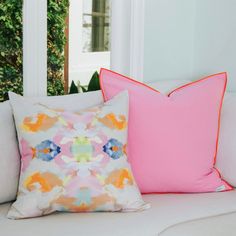 two pink and orange pillows sitting on top of a white couch next to each other