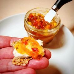 a hand holding a small cracker with food in it and a jar on the side