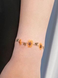 a woman's wrist with three sunflowers attached to the side of her arm