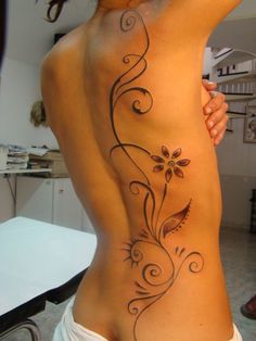 the back of a woman's body with flowers and swirls tattooed on it