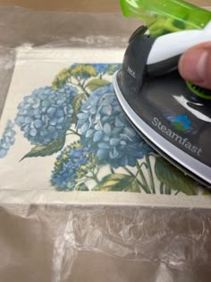 someone using a steam iron on top of a piece of paper with blue and green flowers