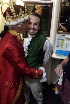 a man in a red and green outfit is hugging another man wearing a crown on his head