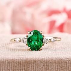 a ring with a green stone surrounded by three white diamonds on a pink flowered cloth