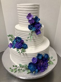 a three tiered white cake with purple and blue flowers