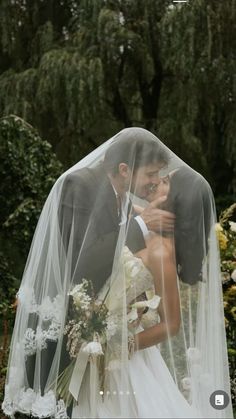 a bride and groom kissing under a veil in front of some trees at their wedding