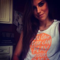 a woman with long brown hair wearing an orange and white shirt that says do one fire can play your game