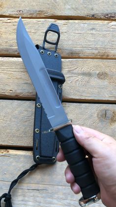 a person holding a knife in front of a black sheath on a wooden table next to a wall