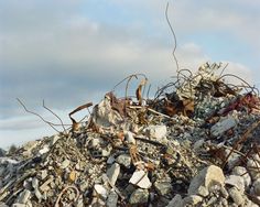 a pile of rocks and debris with grass sticking out of the top, against a cloudy sky