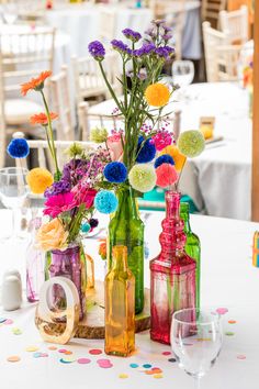 colorful vases filled with flowers on top of a white table cloth covered dining room table