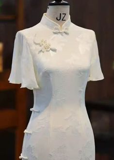 a white dress with flowers on the neck and sleeves is displayed in front of a mannequin