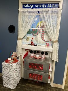 an oven with lights on in front of a christmas themed wall hanging above it is next to a table with presents