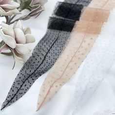 three different colored hair ties sitting on top of a white table cloth next to flowers