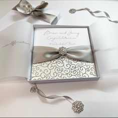 an open box with a silver bow and brooch on it, next to ribbon