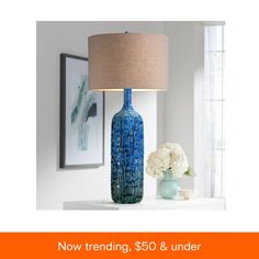 a blue vase sitting on top of a white table next to a lamp and flowers