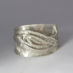 The ancient metal-sculpting method of chasing and repoussé was used to make artwork around the globe, from the mask of Tutankhamun to the Statue of Liberty. This argentium sterling silver cuff bracelet features a sinuous wave-like raised design, comfortable curved edges, and a contoured fit. Chasing and repoussé is a labor-intensive, high-contact process. First, I embed sheet metal in a cast-iron bowl filled with a mixture of pine pitch and brick dust. Using a chasing hammer and a series of specialized steel punches, I gradually push the metal into higher and higher relief, softening it between sessions with high heat as the hammering quickly makes the metal go hard and rigid. It took several days to make this cuff, with multiple sessions of careful sculpting in the pitch bowl followed by Metal Sheet Jewelry, Silver Hand Cast Metal Cuff Bracelet, Silver Metal Cuff Bracelet Hand Cast, Artistic Silver Cuff Bracelet, Unique Sculpted Silver Jewelry, Formal Hammered Silver Cuff Bracelet, Silver Hammered Cuff Bracelet For Formal Occasions, Formal Silver Hammered Cuff Bracelet, Artistic Hammered Silver Jewelry