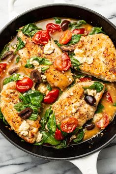 chicken with tomatoes, olives and spinach in a skillet on a marble surface