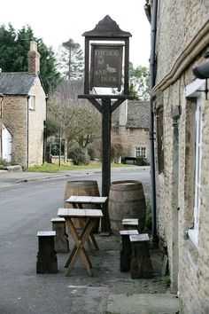 an old fashioned clock on the side of a building next to picnic tables and barrels