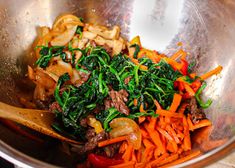 a metal bowl filled with vegetables and meat on top of a wooden spoon in it