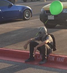 a man sitting on the curb with a green balloon