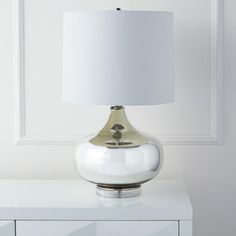 a white table lamp sitting on top of a white dresser next to a white wall