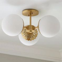 a ceiling light with three white balls hanging from it's center and two gold arms