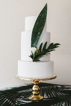 a white wedding cake with greenery on top sits on a gold plated stand