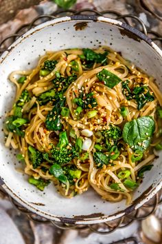 a white bowl filled with noodles, broccoli and seasoning sprinkles