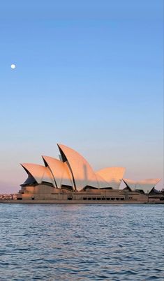 the sydney opera house is lit up at night, as seen from across the water