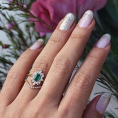 a close up of a person's hand with a ring on it and flowers in the background