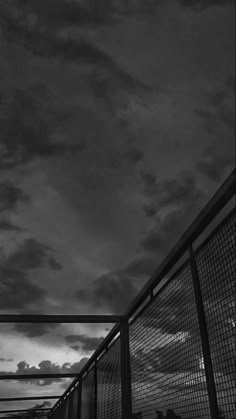 black and white photograph of people walking over a bridge at night with clouds in the background