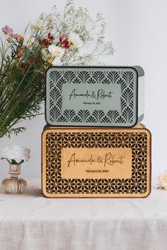 two wooden boxes sitting on top of a table with flowers in the vase behind them