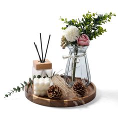 a vase with flowers and candles sitting on a tray next to some pineconis