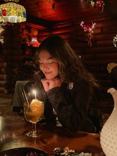 a woman sitting at a table with a lit candle in front of her and other food on the table