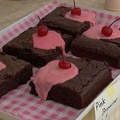 chocolate brownies with pink icing and cherries are on display at the store